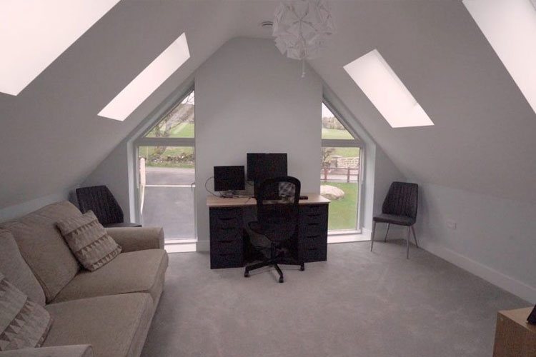 A finished room built into a roof space, with a sloped ceiling meeting at the ridge, a rooflight on each slope and a gable window looking out over fields