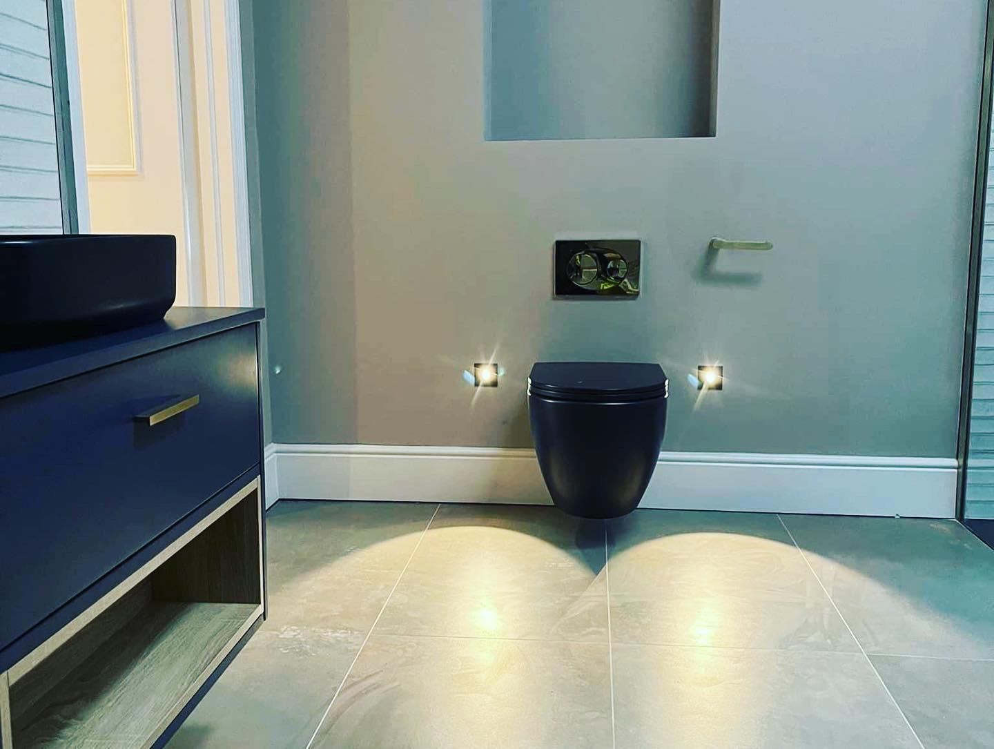 A bathroom with pale teal walls, a navy vanity unit, brass fittings and a wall hung WC