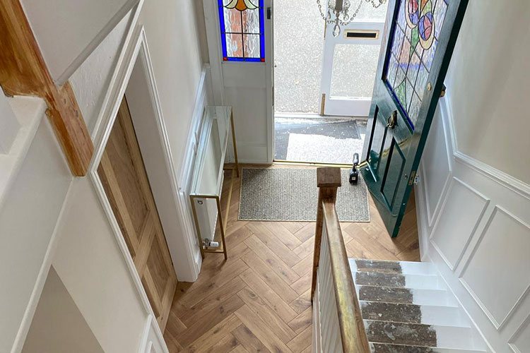 A renovated period hallway with herringbone flooring, panelling and a stained glass door
