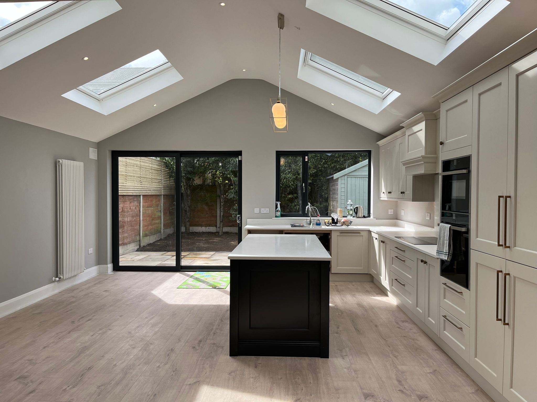 A kitchen under a vaulted ceiling with rooflights, a dark island and glazed doors onto the garden
