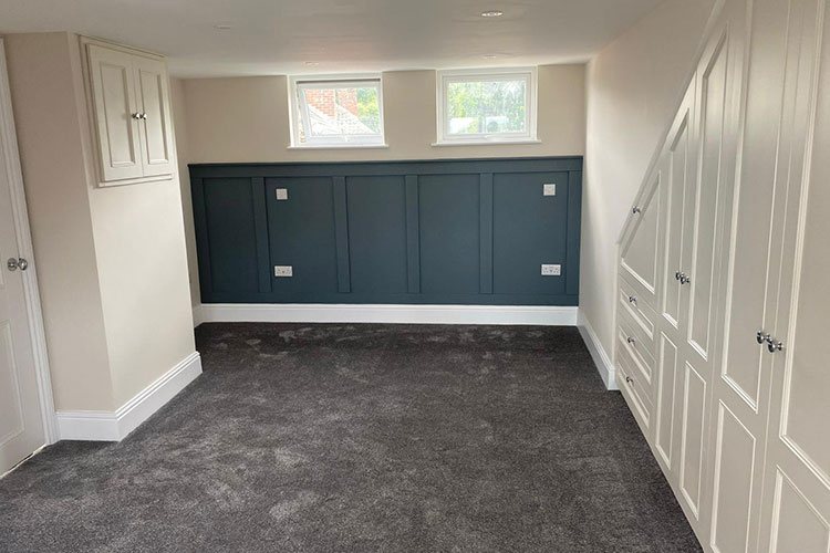 A finished room with fitted wardrobes and dark panelling below a high window